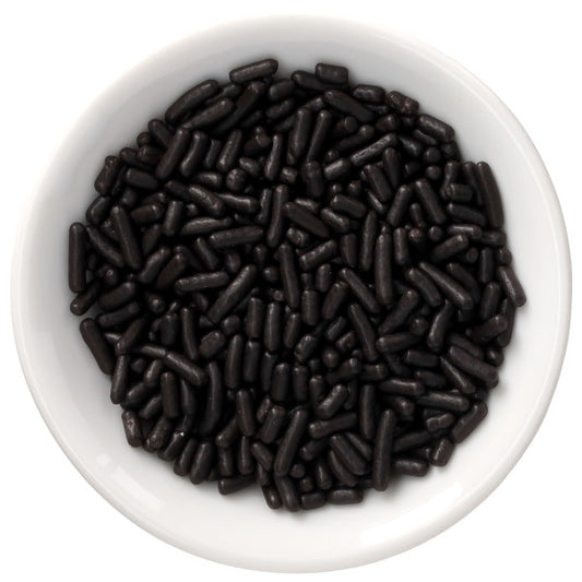 Top-down view of a white bowl filled with black naturally dyed rod-shaped sprinkles on a white background.