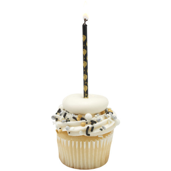 Vanilla cupcake with white frosting, black and gold sprinkles, and a white fondant topper, finished with a lit black candle featuring a gold balloon pattern.