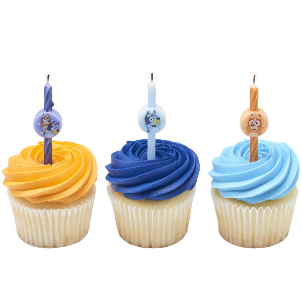 Three vanilla cupcakes with orange, dark blue, and light blue buttercream swirls, each topped with a Bluey character birthday candle.