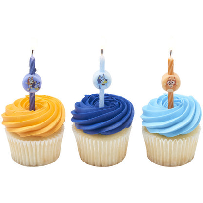 Three vanilla cupcakes with orange, dark blue, and light blue buttercream swirls, each topped with a Bluey character birthday candle.