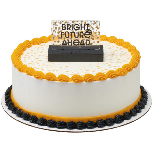 Round white frosted cake with a yellow scalloped top border and black bottom border, topped with a “BRIGHT FUTURE AHEAD” confetti sign in a black base at the center.