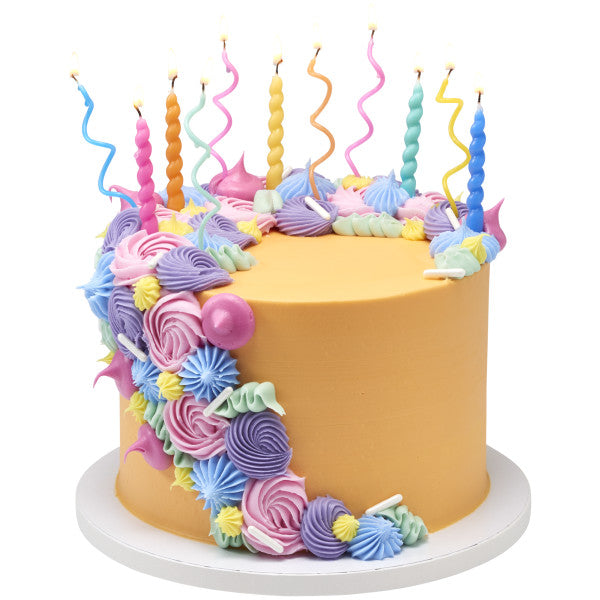 Round cake with smooth golden frosting and a cascade of pastel buttercream swirls, topped with bright twist candles and wavy spiral candles in multiple colors.