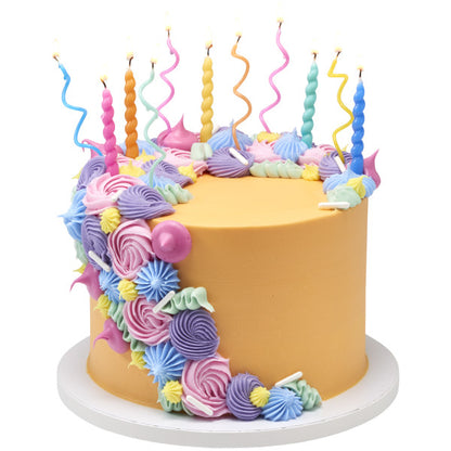 Round cake with smooth golden frosting and a cascade of pastel buttercream swirls, topped with bright twist candles and wavy spiral candles in multiple colors.