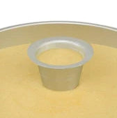 Aluminum cake heating core with a hollow center tube, shown inserted into the middle of a large round cake batter-filled pan to help the center bake evenly.