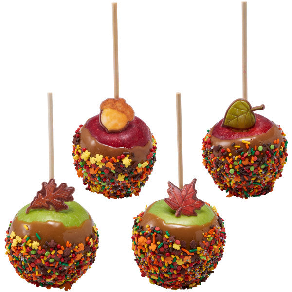 Four caramel-dipped apples coated with colorful autumn sprinkles, each topped with decorative fall-themed fondant toppers like leaves and acorns.