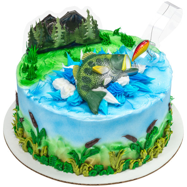 A round cake decorated with a fishing pond theme, showcasing the fish figurine, fishing line with bait, and forest background.