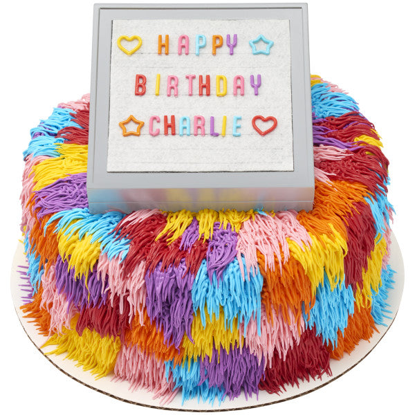 Round cake with a fluffy multicolored frosting design and letter board topper displaying a birthday message.