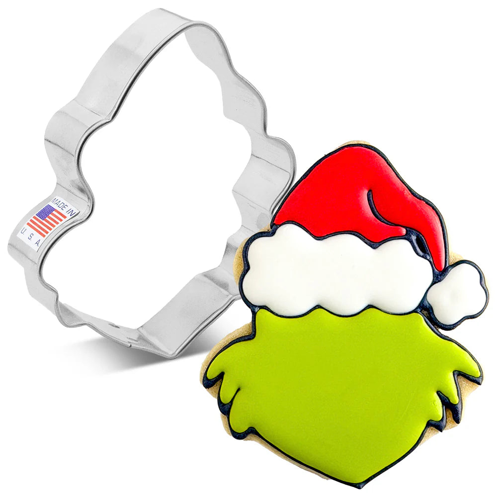 Silver Christmas grump with Santa hat cookie cutter shown next to a decorated cookie with bright green face icing, white hat trim, and a red Santa hat outlined in dark icing on a white background.