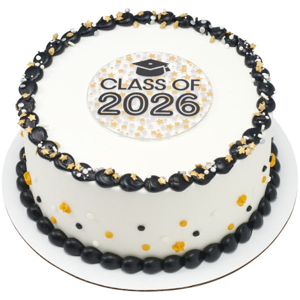 White frosted round cake with a black piped border and gold star sprinkles, topped with a round Class of 2026 confetti layon at the center.