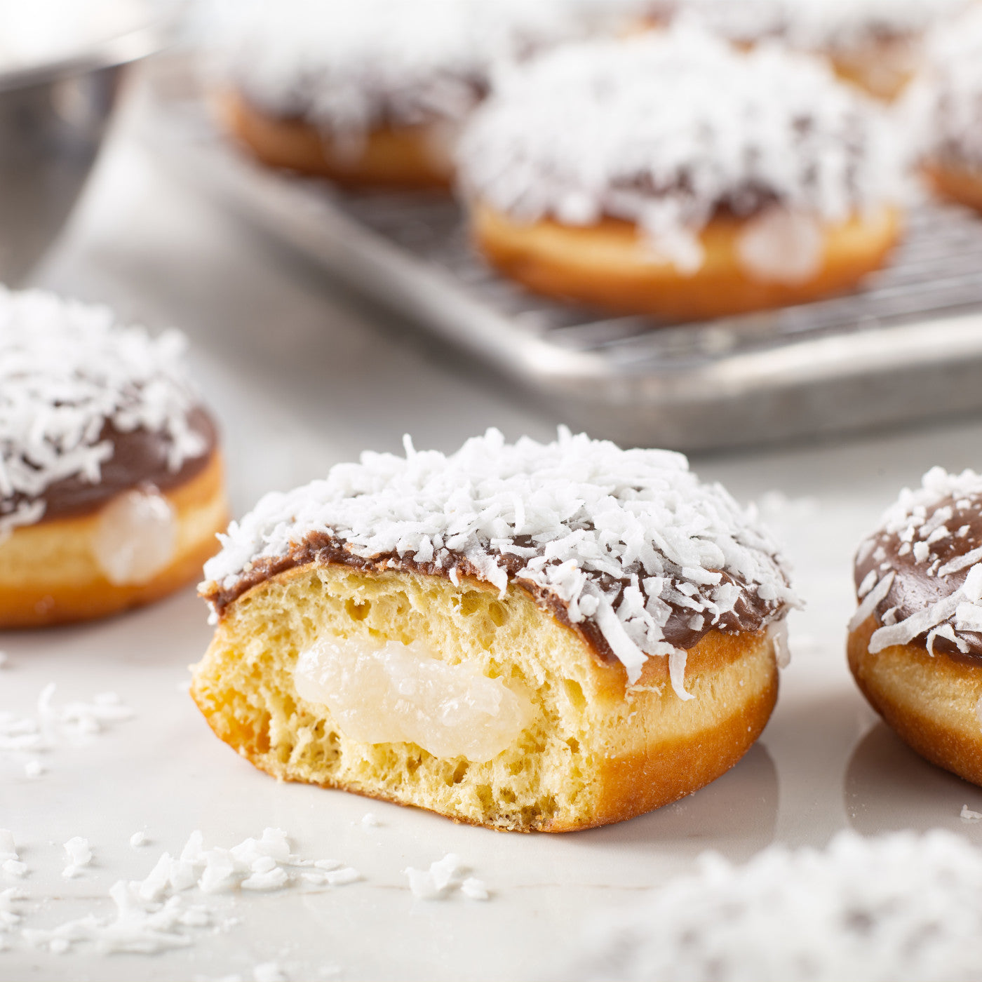 Donut filled with coconut pastry filling, topped with chocolate icing and shredded coconut; sliced to show interior