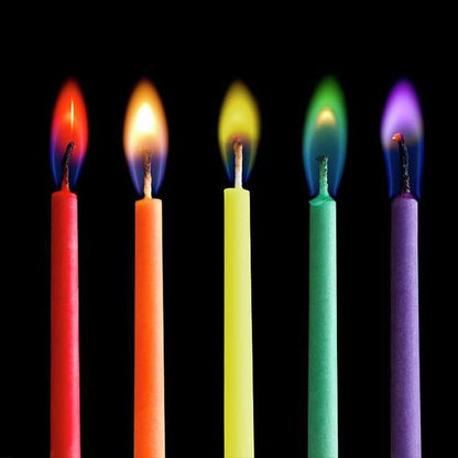 Five lit birthday candles with vibrant flames in red, orange, yellow, green, and purple against a dark background.