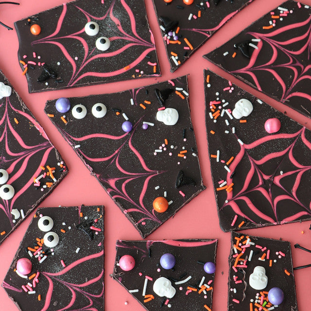 Halloween-themed chocolate bark tinted with Colour Mill Black, decorated with pink spiderweb piping, candy eyes, and colorful sprinkles