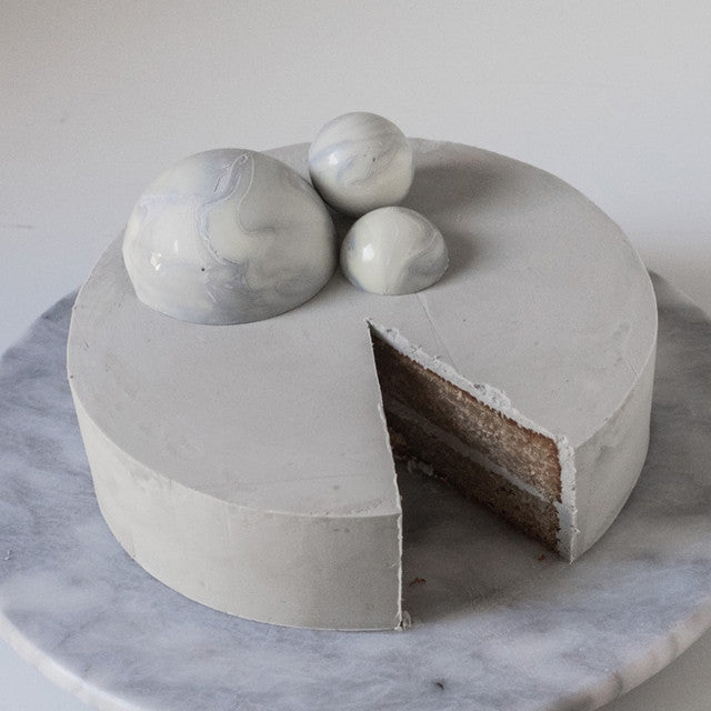 Minimalist cake covered in grey buttercream with marbled chocolate spheres, colored using Colour Mill Concrete.