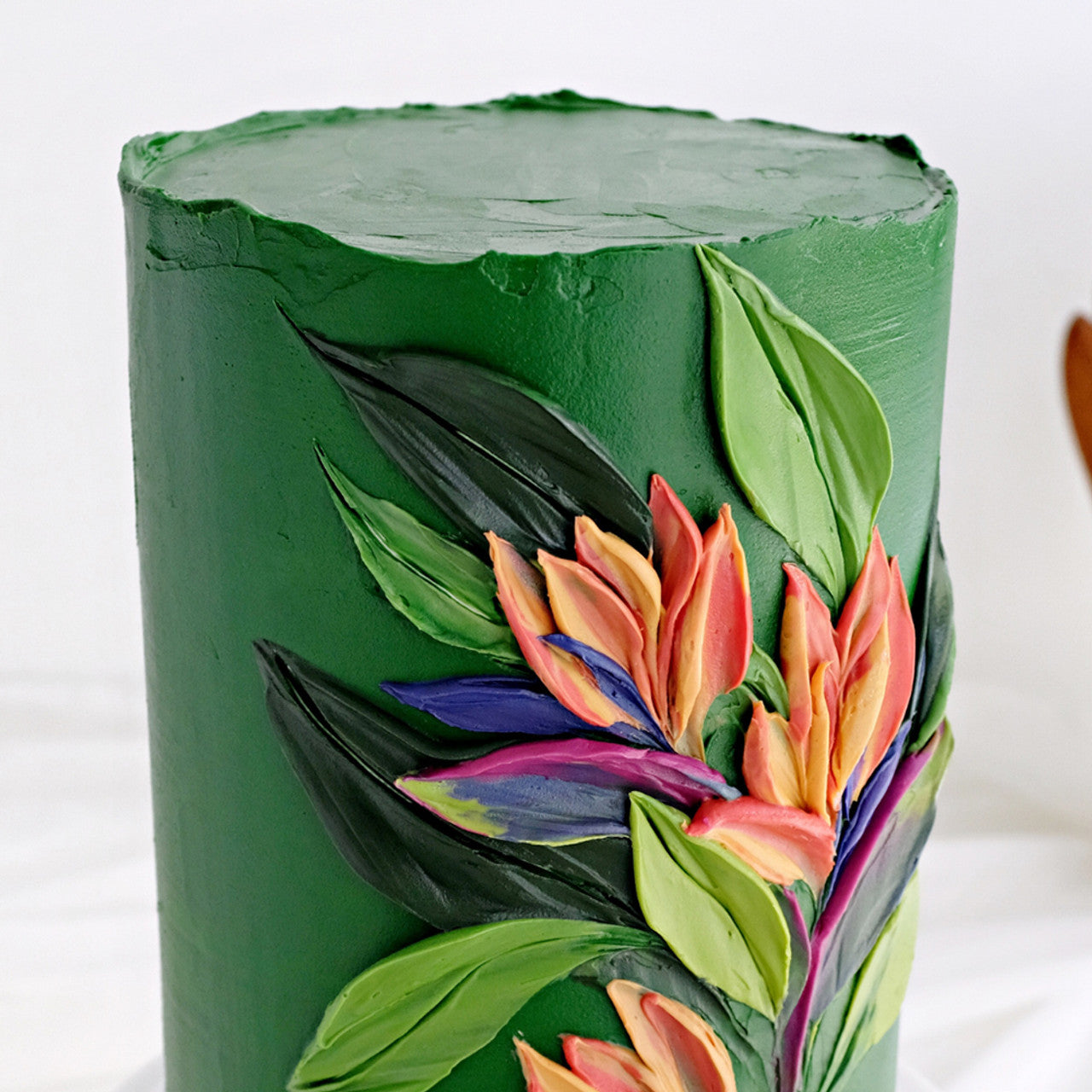 Tall cake decorated with deep green frosting and vibrant buttercream floral designs.