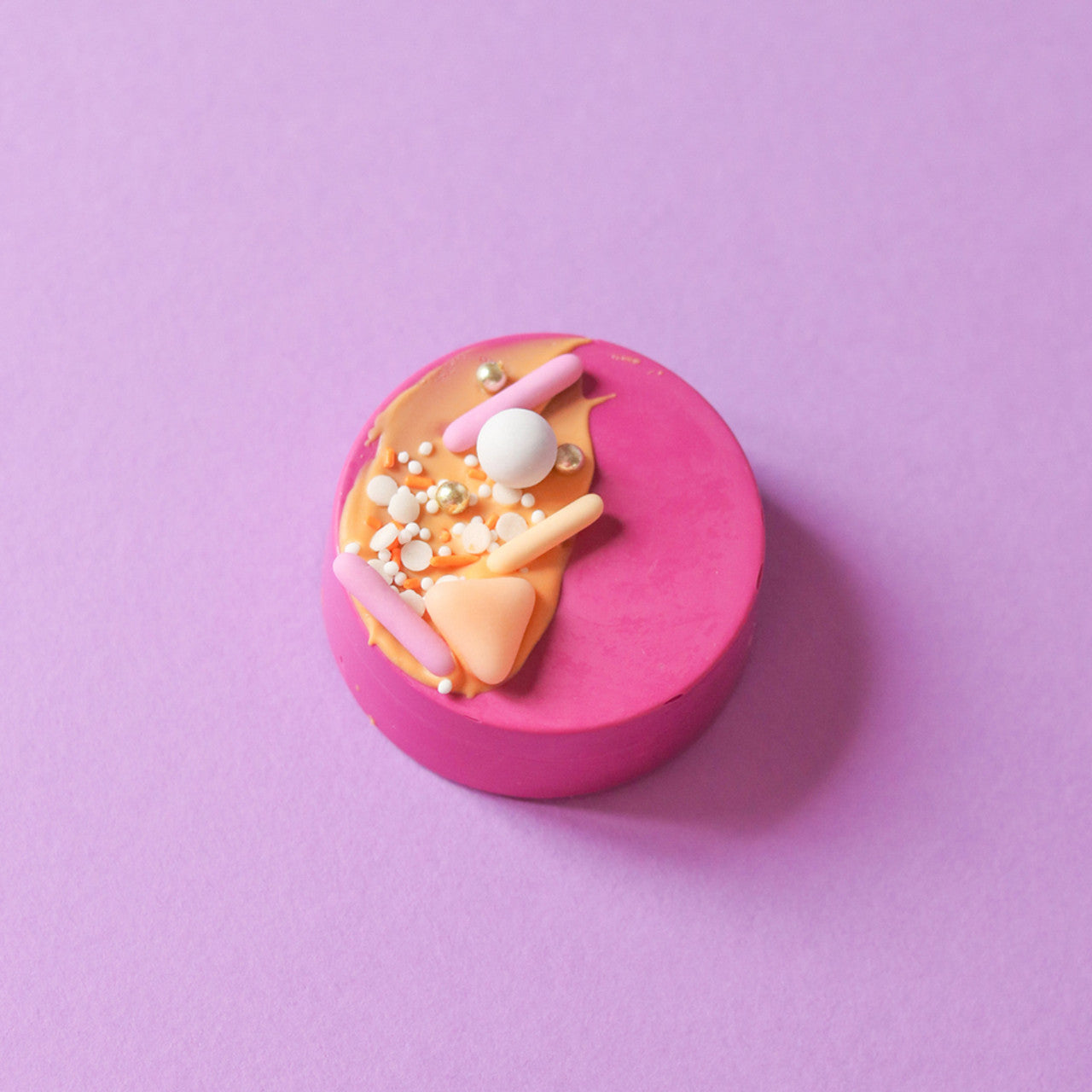 Dessert covered in fuchsia coating, topped with pastel and metallic sprinkles.