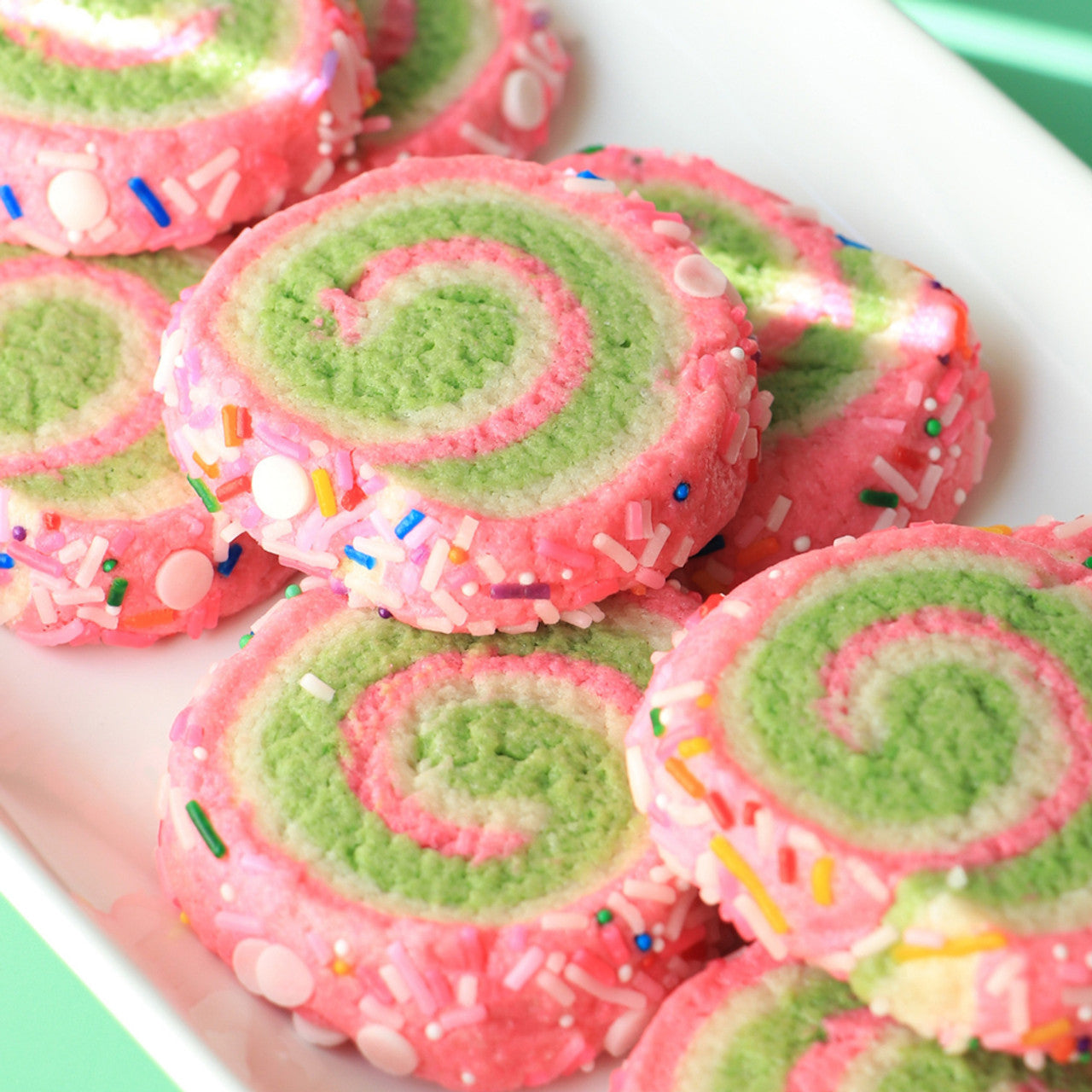 Spiral cookies decorated with Colour Mill Lime and pink coloring, covered in rainbow sprinkles.