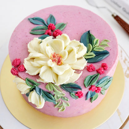 Decorated buttercream cake with piped white and red flowers and raspberry-toned frosting using Colour Mill Raspberry.