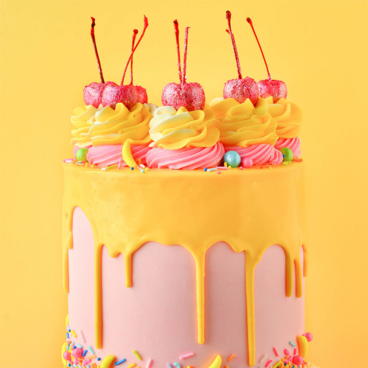 Colorful layered cake with yellow drip, yellow and pink swirls, and cherry toppers using Colour Mill Yellow coloring