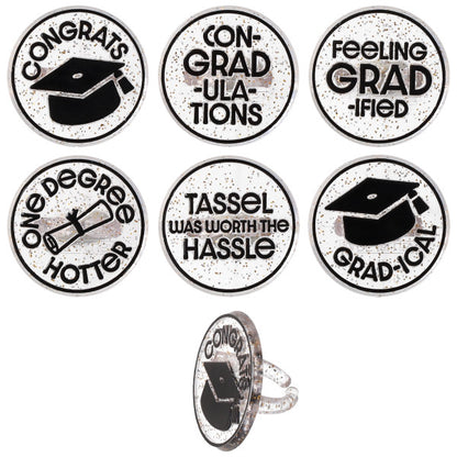Six confetti graduation cupcake rings with black-and-white designs and phrases like “Congrats,” “Con-grad-ulations,” and “Tassel was worth the hassle,” shown on a white background with one ring displayed from the side.