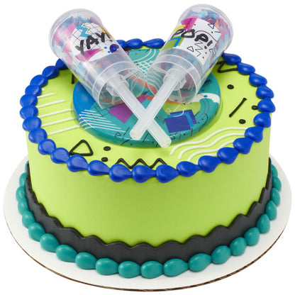 A round cake with bright green, blue, and black icing, topped with the confetti launchers and geometric base.