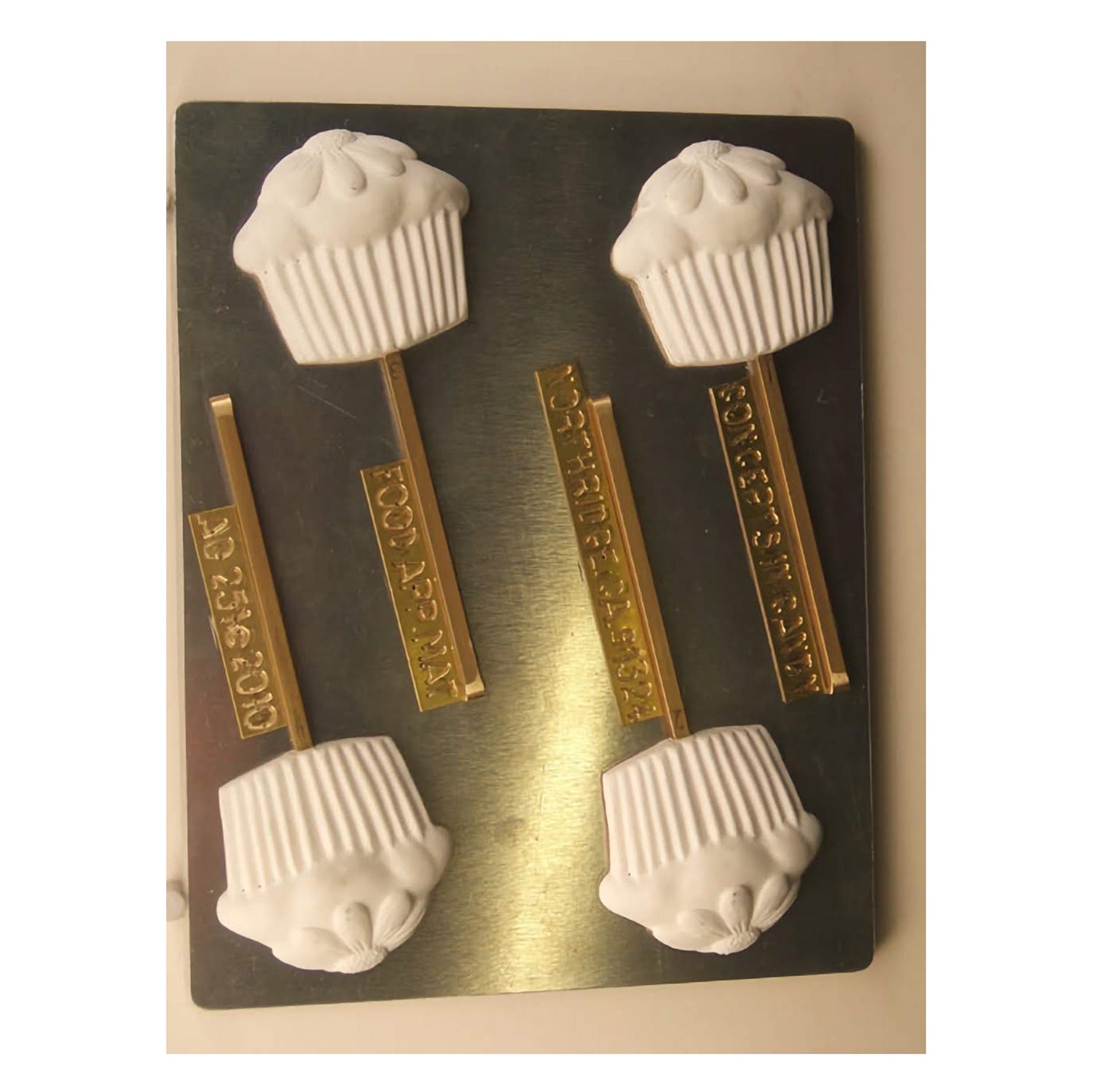 This image shows a chocolate mold used for making cupcake-shaped lollipops. The mold has three cavities, each designed to shape chocolate into a cupcake with a daisy on top