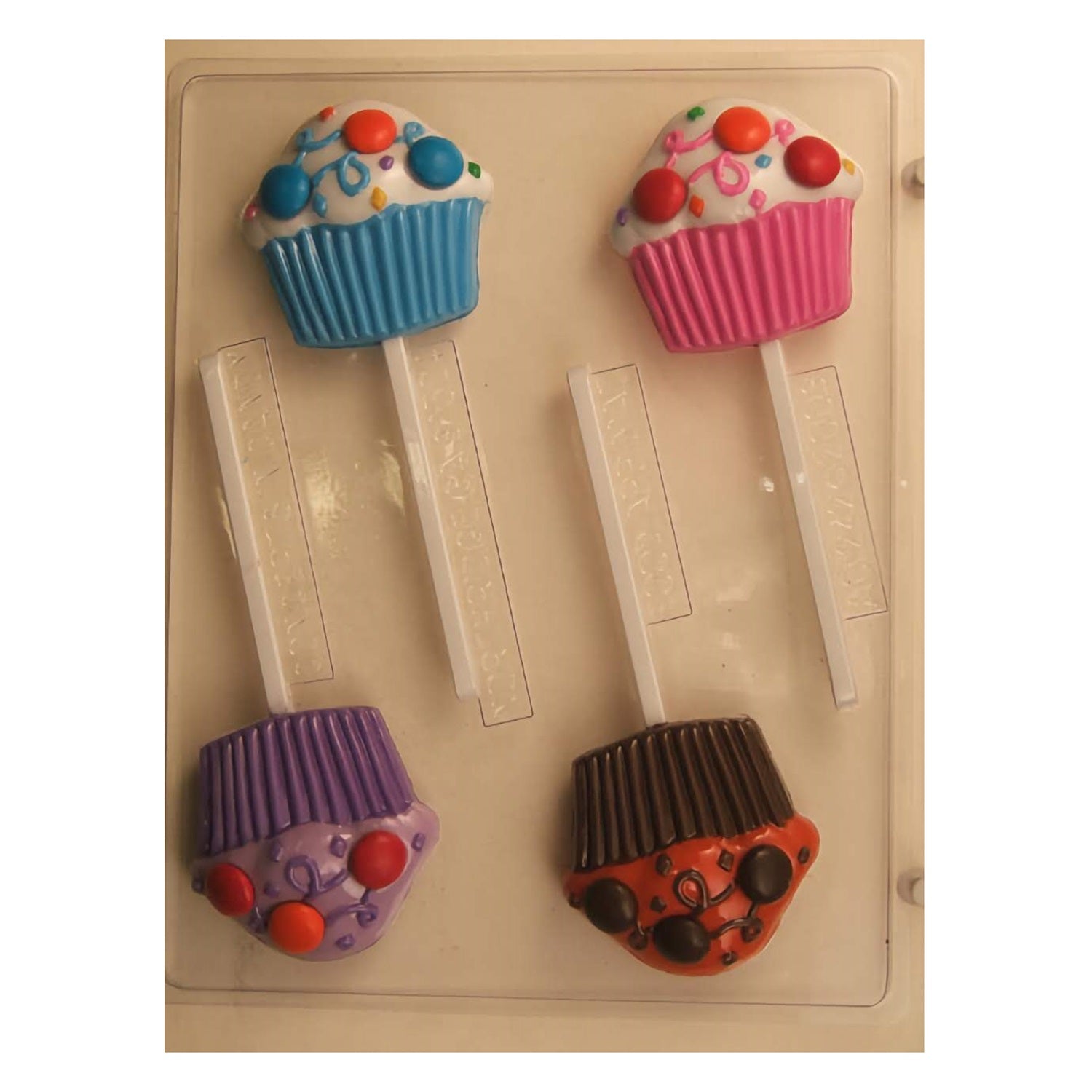 This chocolate mold has four cavities shaped like decorative cupcakes topped with swirls and confetti details, each with a stick insert to create festive lollipop treats.