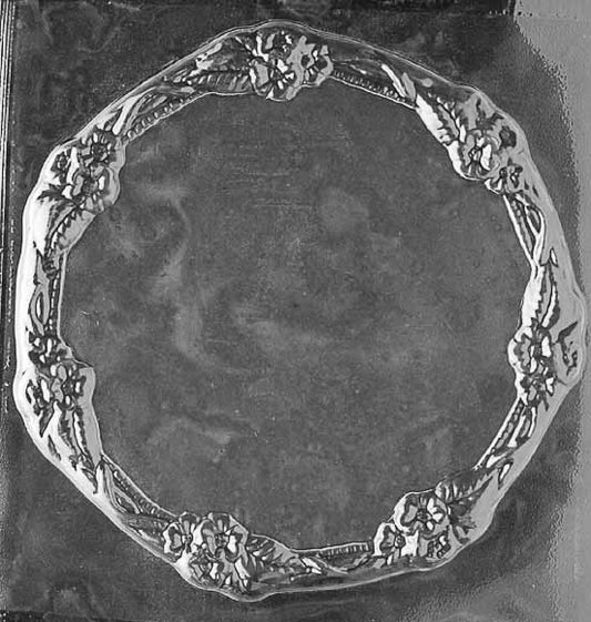 Chocolate mold shaped like a round plate with floral border detailing and shallow depth.