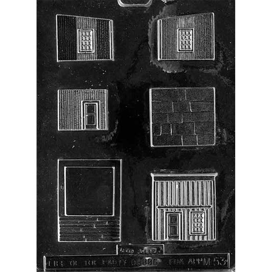 Clear plastic chocolate mold with multiple building panel cavities for a store front, including a storefront face with door and window shapes, siding-textured wall pieces, a shingled panel, and a rectangular base piece.