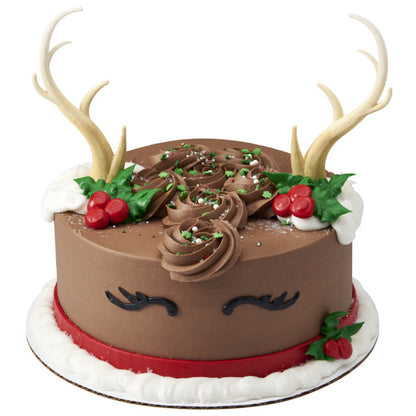 Reindeer-themed holiday cake with chocolate frosting, holly decorations, and deer antler toppers.