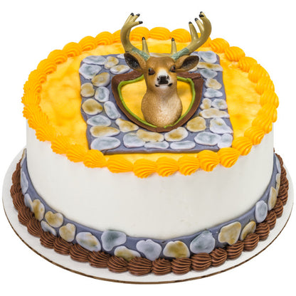 A round cake decorated with a hunting lodge-inspired design, featuring a deer head topper mounted on a stone-like plaque.