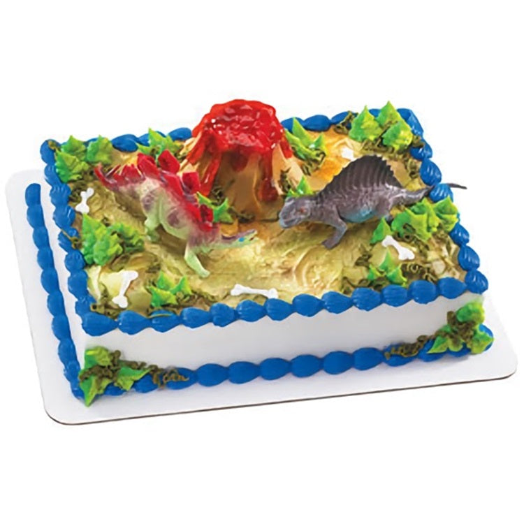 A rectangular cake topped with a dynamic dinosaur scene, showcasing red, green, and purple dinosaur figurines, a fiery red volcano, and lush green frosting foliage, perfect for dinosaur-themed parties and Jurassic aficionados.