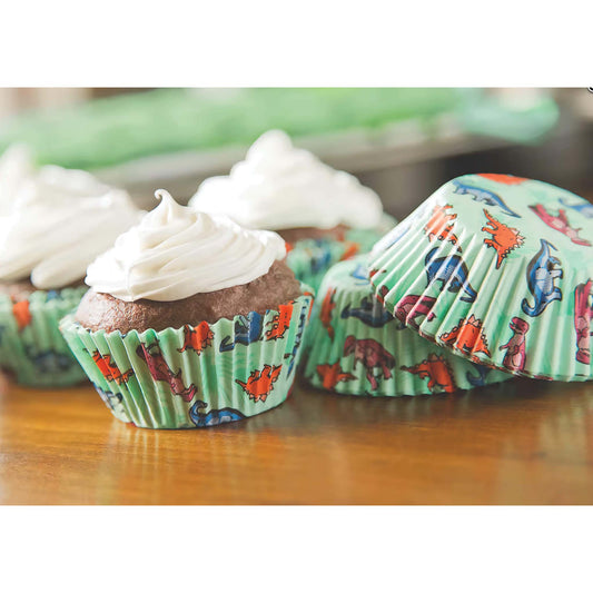 Chocolate cupcakes with white frosting in dinosaur-themed baking cups on a wooden surface.