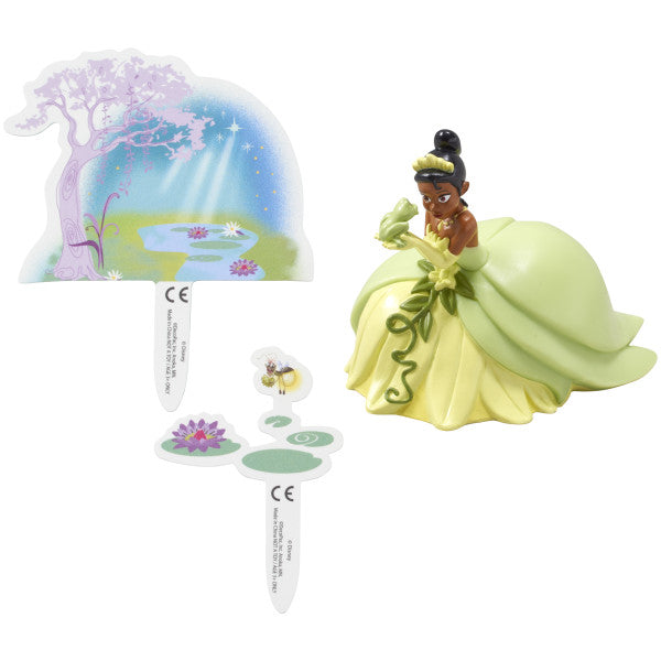 A kneeling Tiana figurine holding a frog, alongside two decorative pop-up scenery pieces.