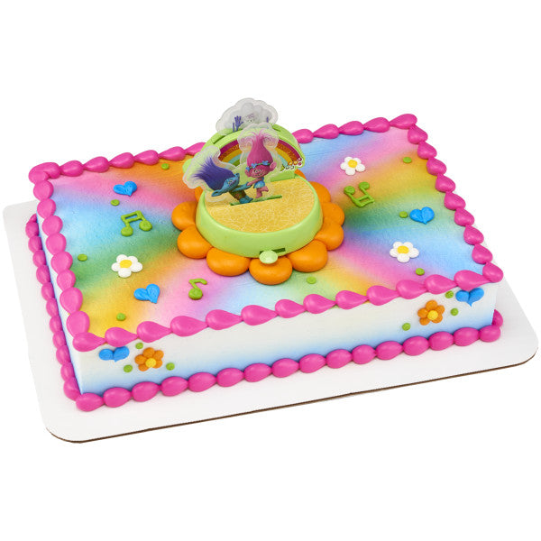 A rectangular cake decorated with the Trolls DecoSet®, featuring a rainbow-colored background and fun musical notes.