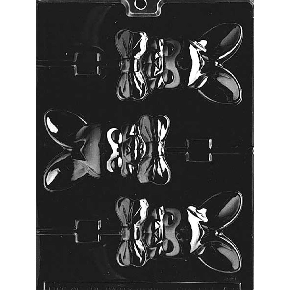 Clear plastic chocolate lollipop mold with three cavities shaped like a bunny head with tall upright ears and a large bowtie under the face, each cavity connected to a lollipop stick channel on a dark background.
