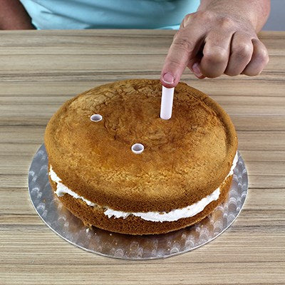 Close-up of dowel rods being inserted into a cake layer for structural support during cake stacking.