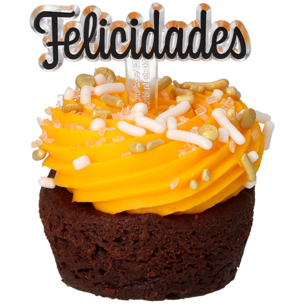 Cupcake de chocolate con betún amarillo en espiral y sprinkles variados, decorado con un pick que dice “Felicidades” en letras negras.