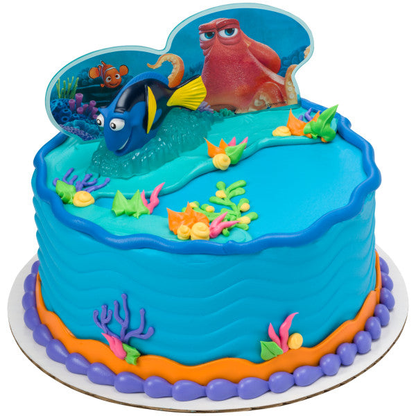 A round cake with bright blue frosting and ocean-themed decorations, showcasing the Finding Dory cake topper set with coral accents.