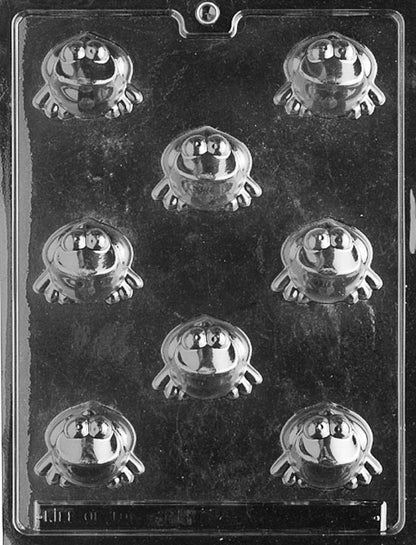Clear chocolate mold with eight round frog cavities featuring big eyes and small feet, arranged in rows on a glossy plastic sheet against a dark background.