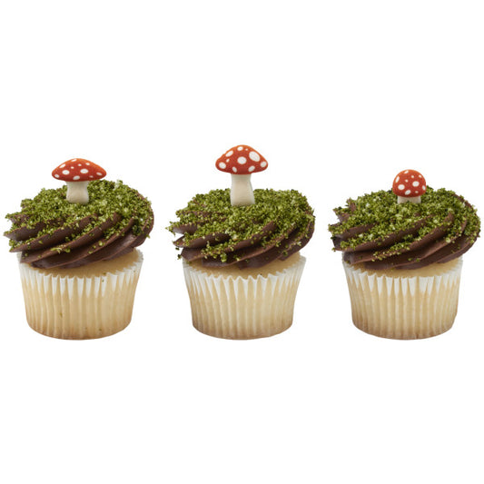 Three vanilla cupcakes with chocolate frosting swirls topped with green crumb “moss” and a small red-and-white pressed sugar mushroom decoration on each cupcake.
