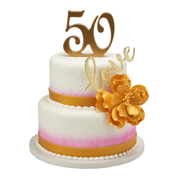 A two-tiered white cake decorated with gold accents, a floral embellishment, and a gold "50" topper, perfect for a 50th anniversary or birthday celebration.