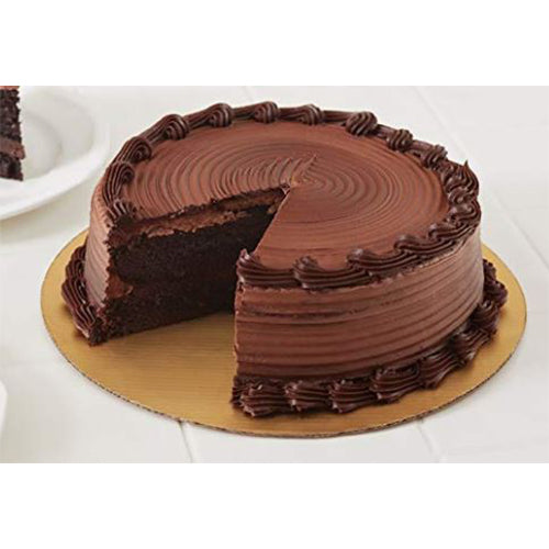 Round chocolate frosted cake with piped borders and a slice removed, displayed on a gold round cake board on a white table.