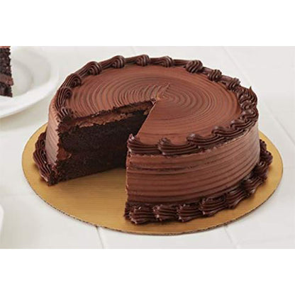 Round chocolate frosted cake with piped borders and a slice removed, displayed on a gold round cake board on a white table.