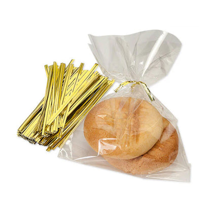 Gold metallic twist ties beside a clear cellophane treat bag tied at the top, holding two round cookies on a white background.