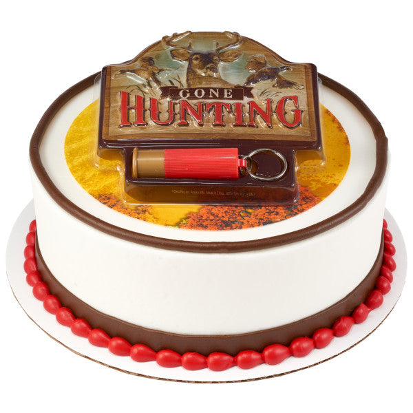 Round white cake decorated with red and brown icing accents and topped with a Gone Hunting cake topper plaque and red cartridge shell keychain.