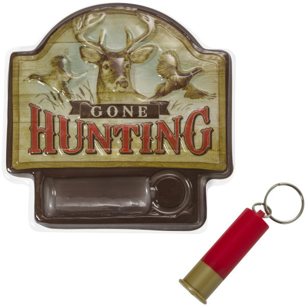 Close-up of the Gone Hunting cake topper plaque with rustic woodland artwork, deer and bird imagery, and a red plastic cartridge shell keychain.