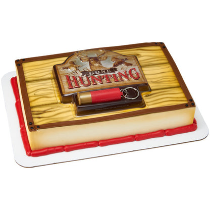 Sheet cake with wood-grain style icing topped with a Gone Hunting plaque cake topper and red cartridge shell keychain, finished with red and brown borders.