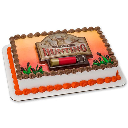 A rectangular cake decorated with a 'Gone Hunting' theme, including a detailed shotgun shell, a hunting dog figurine, and a sign, finished with orange and brown frosting details, perfect for hunting enthusiasts and outdoor-themed events.