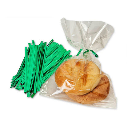 Green metallic twist ties beside a clear cellophane treat bag tied at the top, holding two round cookies on a white background.