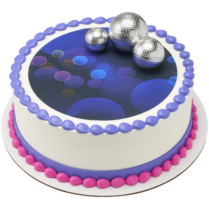 A round cake featuring a dark blue edible image with glowing lights, bordered in purple and pink frosting, with the Groovy Disco DecoSet disco balls on top.